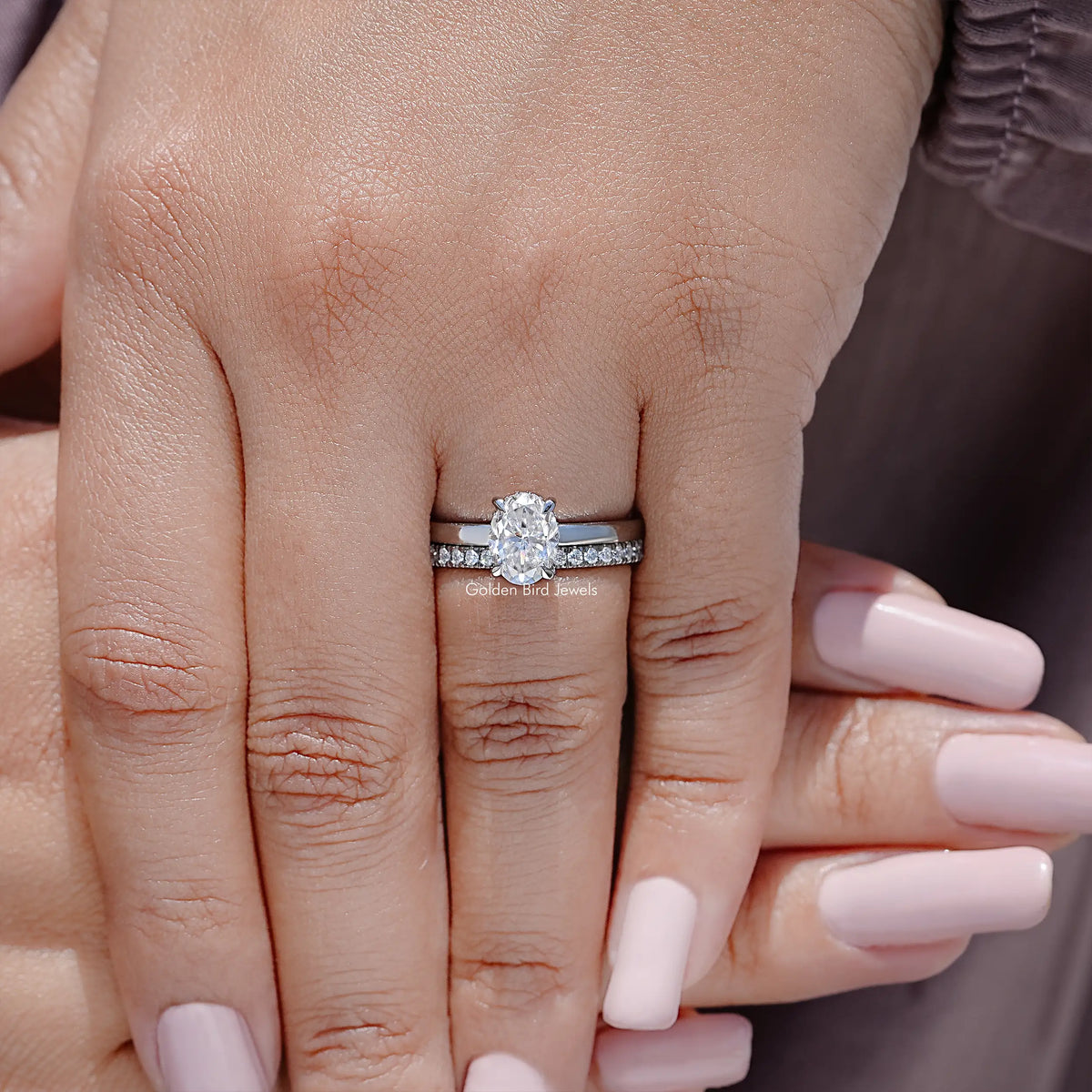 Oval-cut moissanite bridal ring set with halo and pavé band on a finger