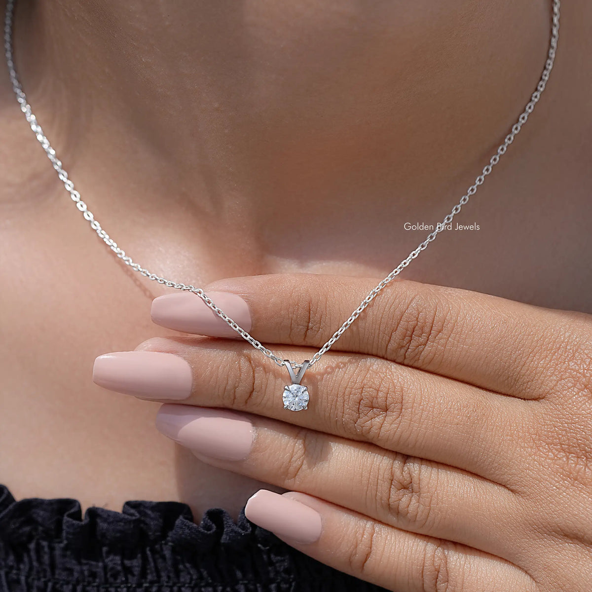Silver moissanite solitaire pendant with round stone on chain, resting across fingers