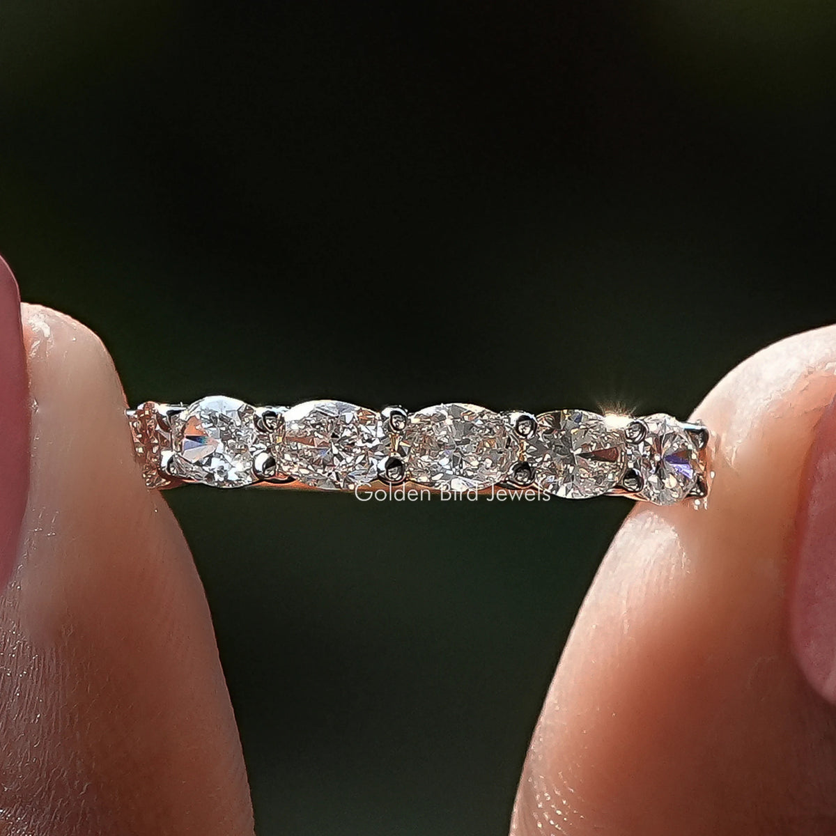 East West Oval Diamond Eternity Wedding Band Held Between Fingers