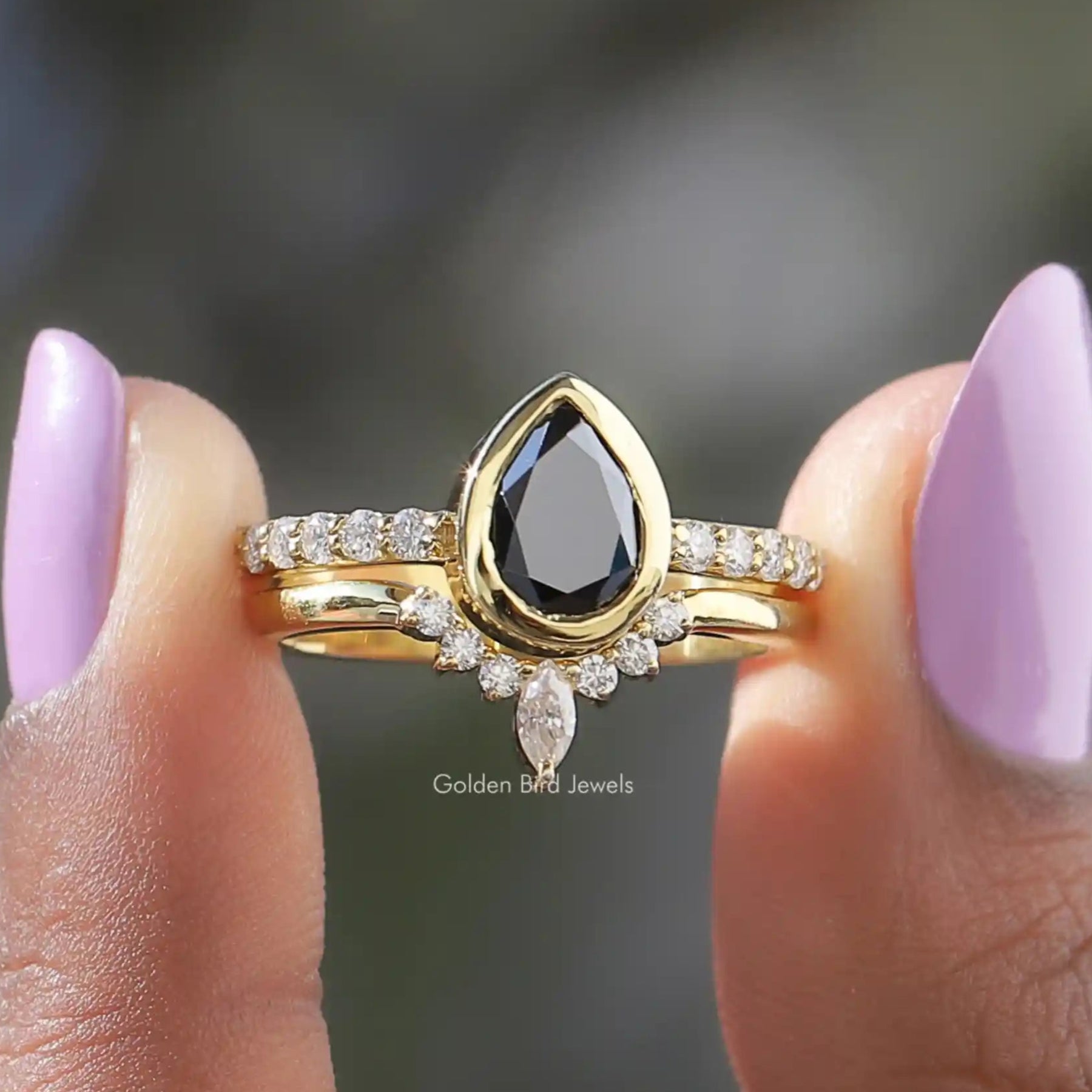 Two fingers holding the Black Pear Cut Moissanite Bridal Ring Set