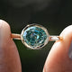 Front view of Blue Green Moissanite Step Cut Oval Solitaire Ring in two fingers 
