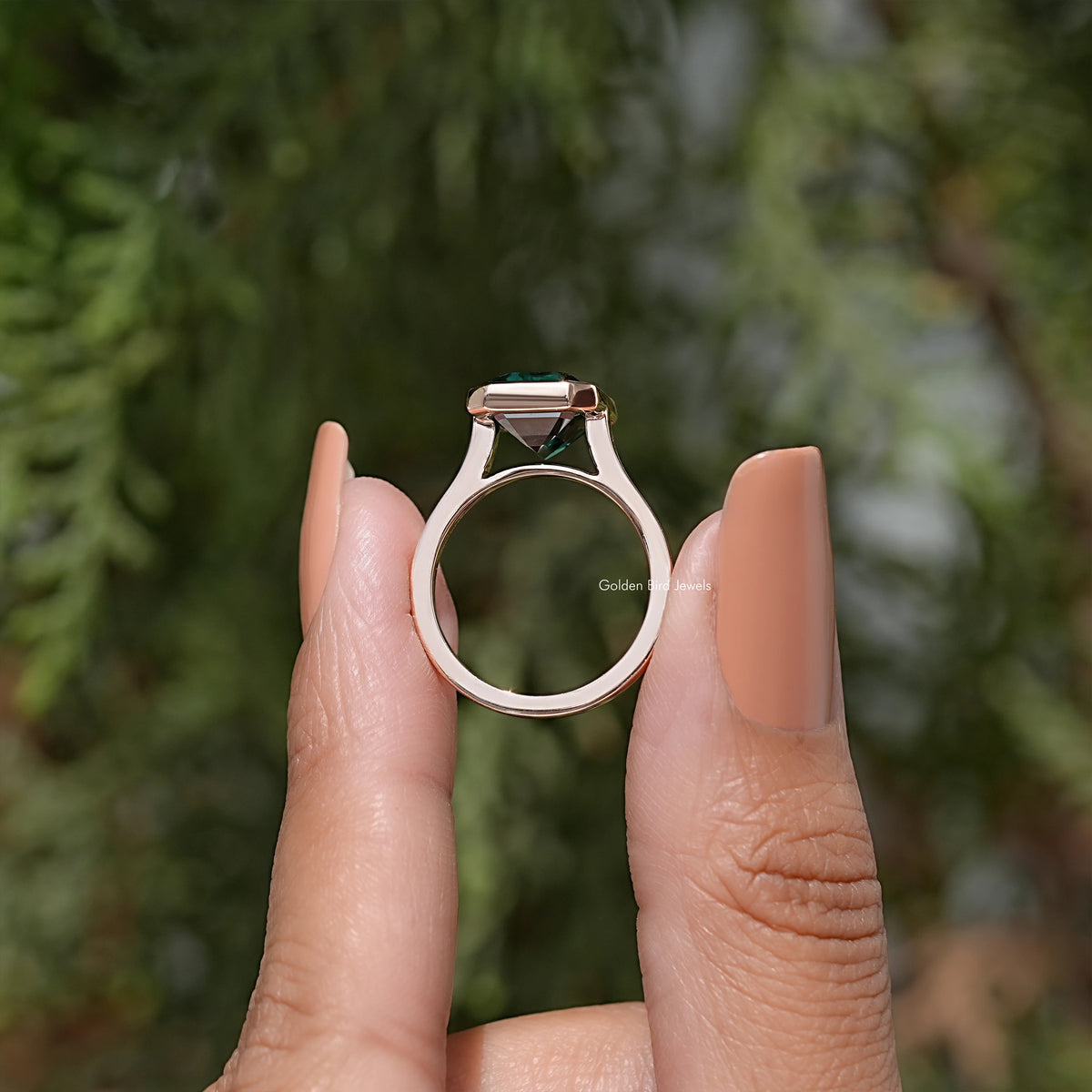 Emerald green moissanite solitaire ring viewed from side, rose gold-tone band
