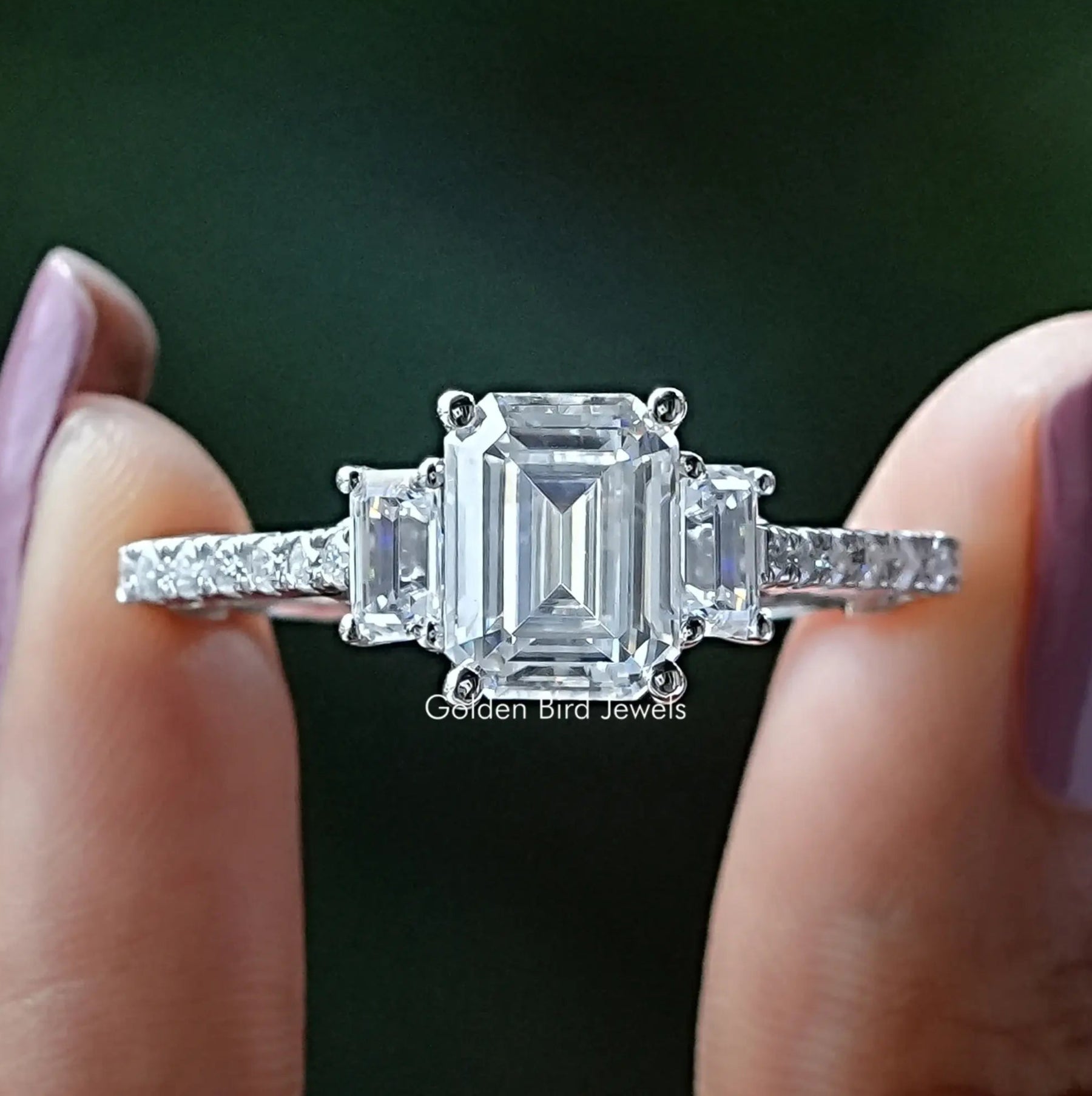Front View of Emerald Cut Three Stone Moissanite Engagement Ring In two Fingers