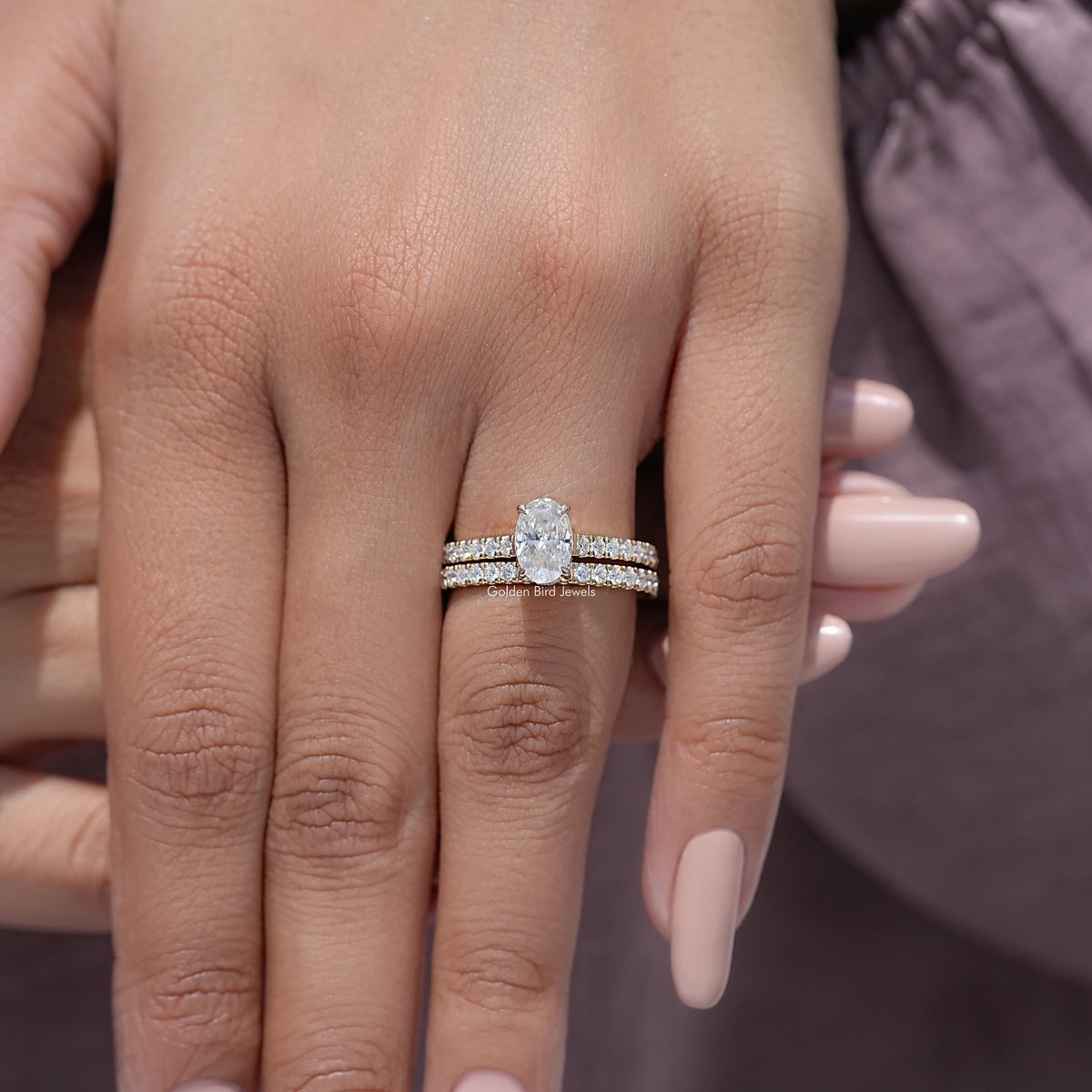 Oval-cut moissanite wedding ring set in a stacked silver-toned design on a hand