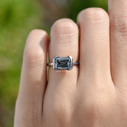 East-west moissanite solitaire ring with half bezel setting on a sterling silver band