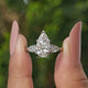 Three Stone Pear Shaped Diamond Engagement Ring Held Between Fingers