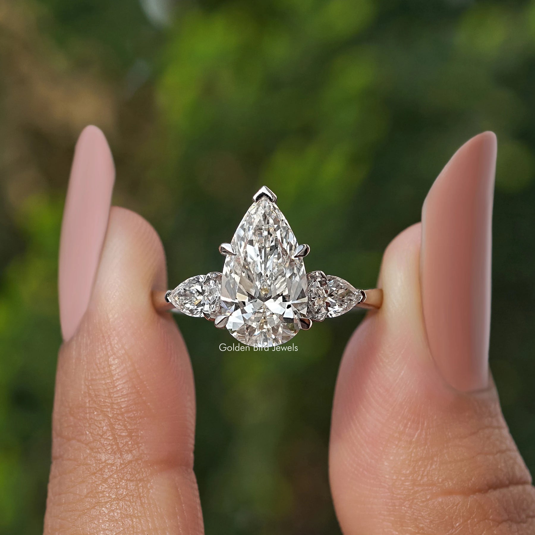Three Stone Pear Shaped Diamond Engagement Ring Held Between Fingers