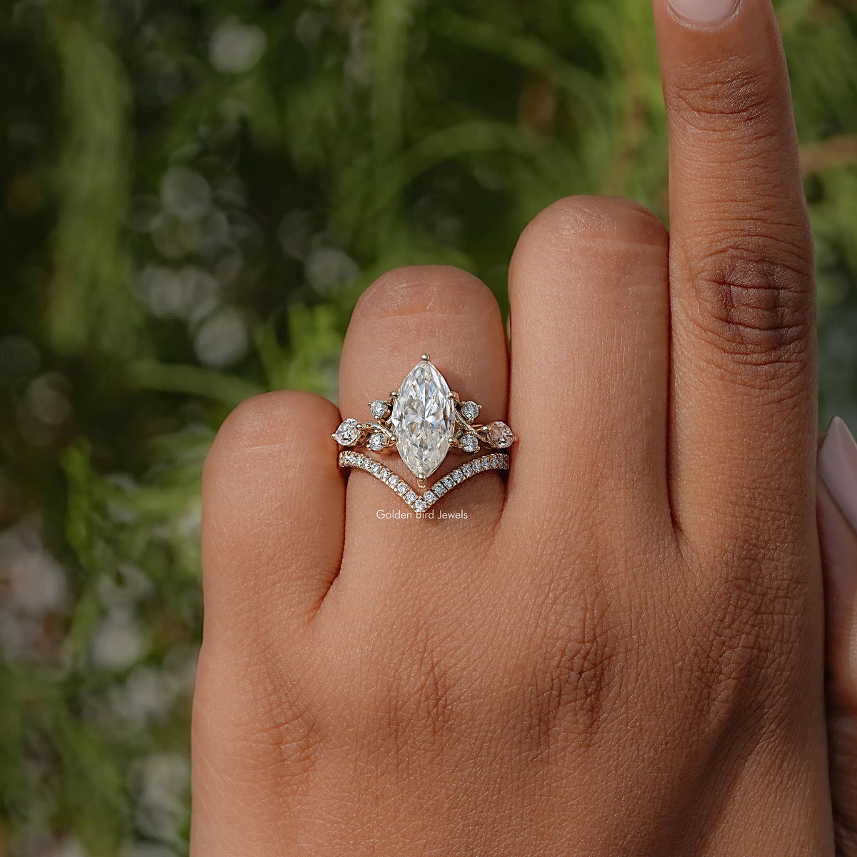 Gold-tone marquise cut cluster engagement ring on finger with prong-set center stone