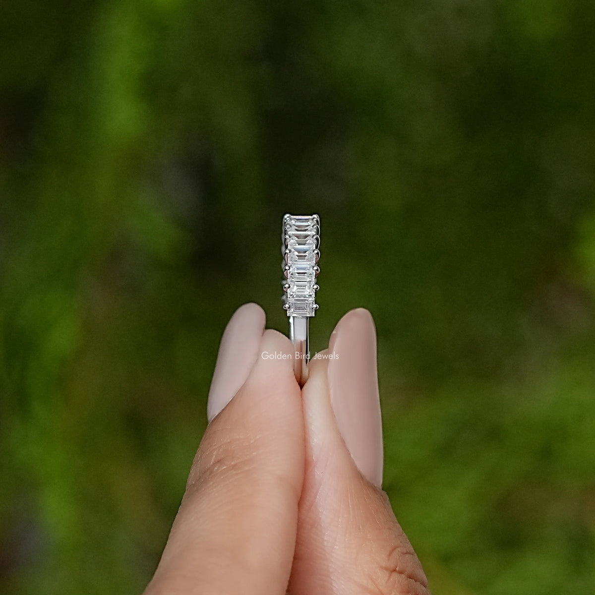 Silver baguette-cut half-eternity band, front view held between fingers