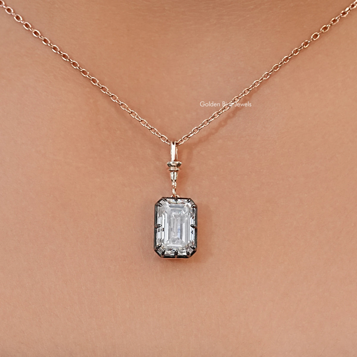 Solitaire pendant necklace with a clear emerald-cut stone, dark setting, and fine chain