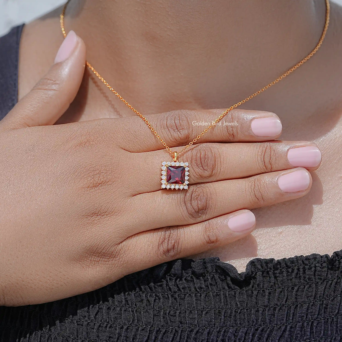 Close-up of square ruby-red pendant with clear halo stones on gold chain