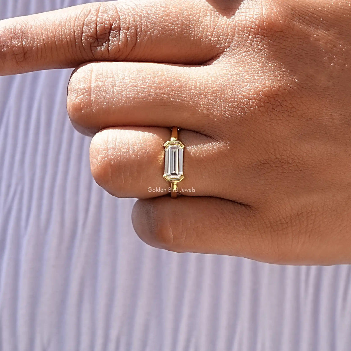 Emerald-cut east-west solitaire ring close-up, gold-tone bezel and prongs