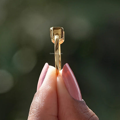 Emerald-cut east-west solitaire ring profile view, gold-tone prongs and band