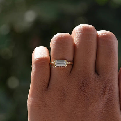Emerald-cut solitaire ring in east-west orientation on hand, gold-tone band